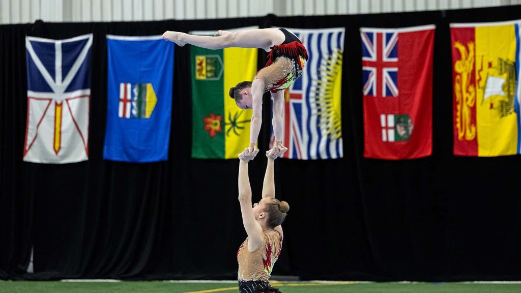 A female gymnast does the splits while holding another gymnast in the air with her hands at the 2024 Canadian Gymnastics Championships